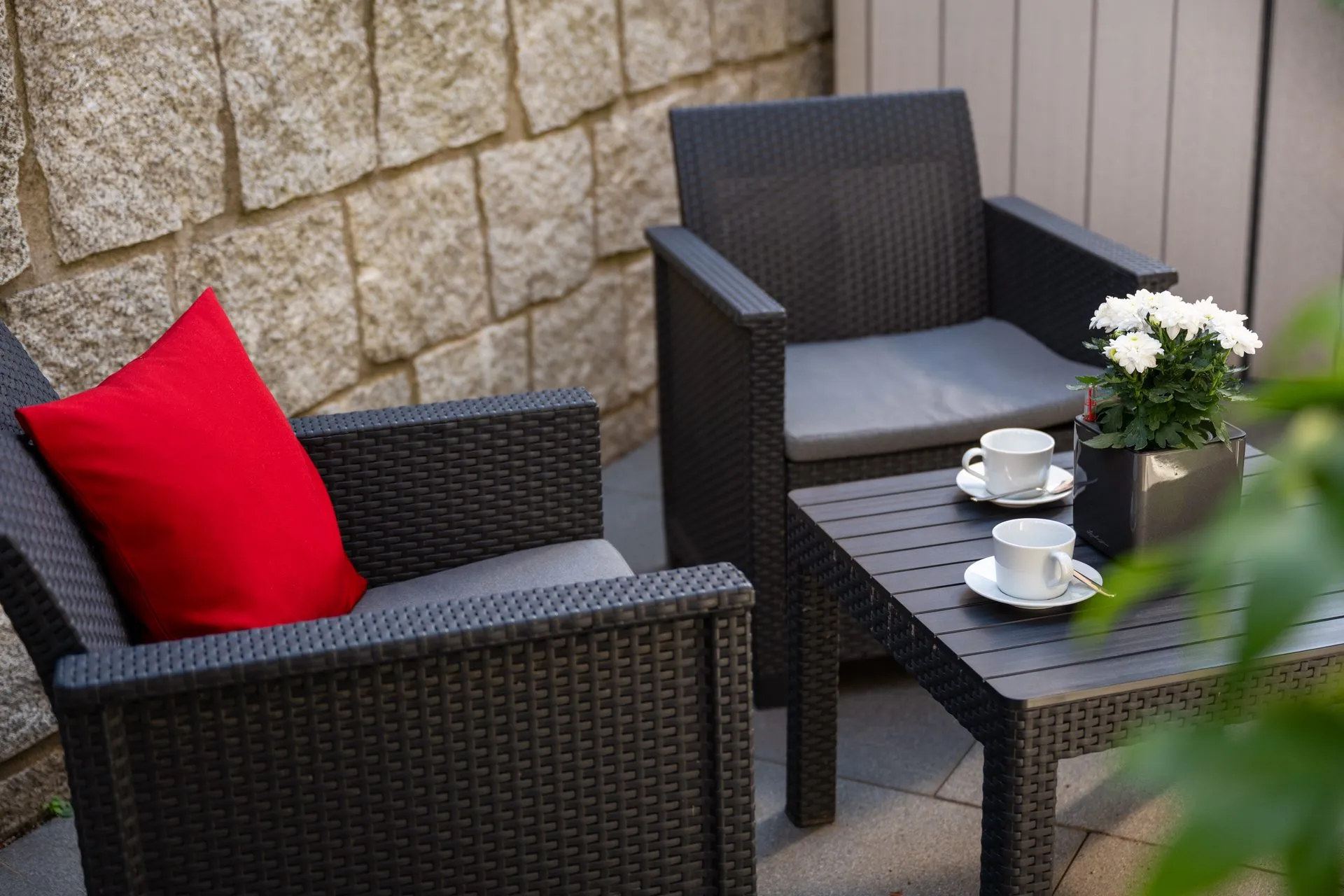 Balkon mit Korbsessel, rotem Kissen und gedecktem Kaffeetisch