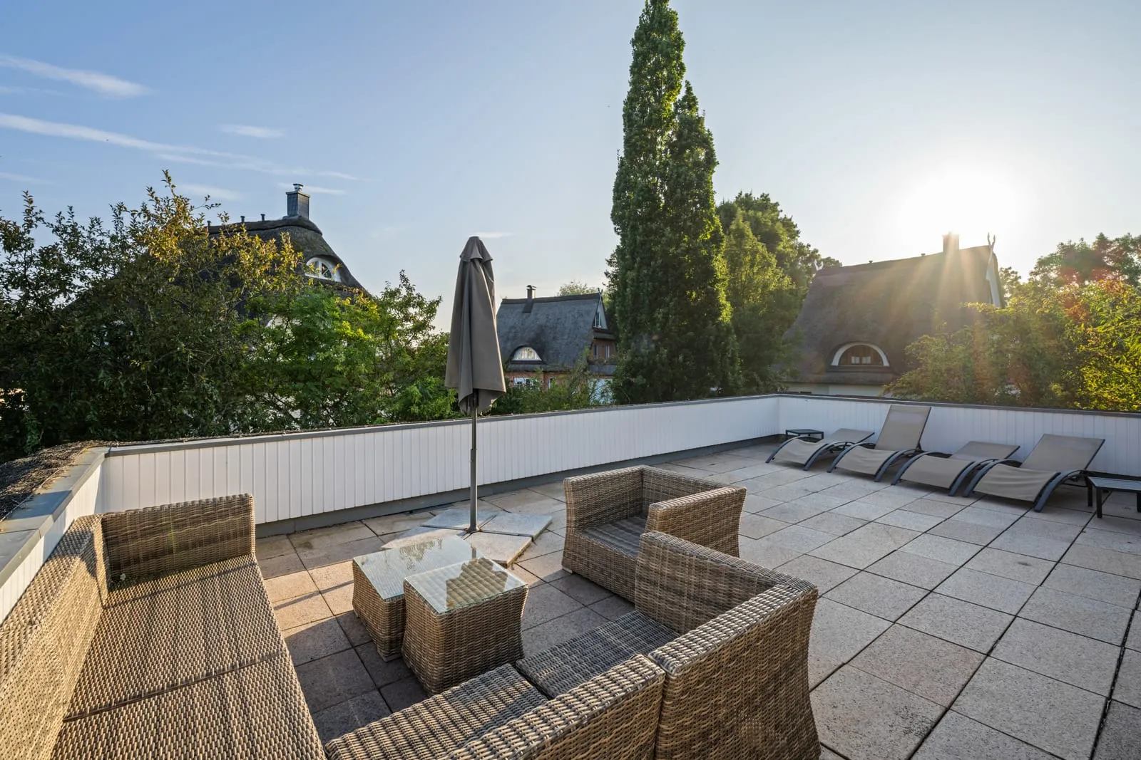 Dachterrasse vor dem Styling – unbestückte Rattanmöbel und geschlossener Sonnenschirm im harten Mittagslicht