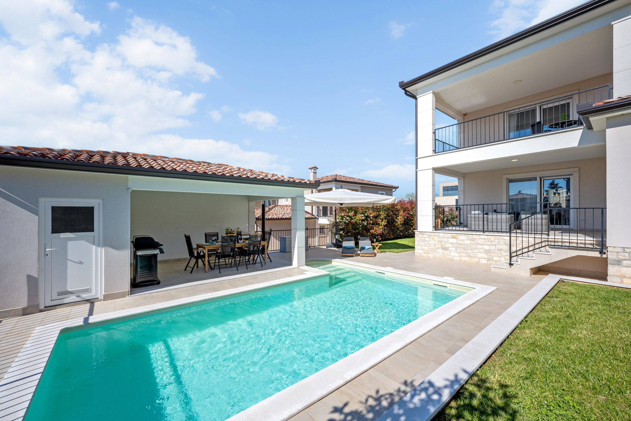 Pool area of the villa by day with a covered seating nook and grill