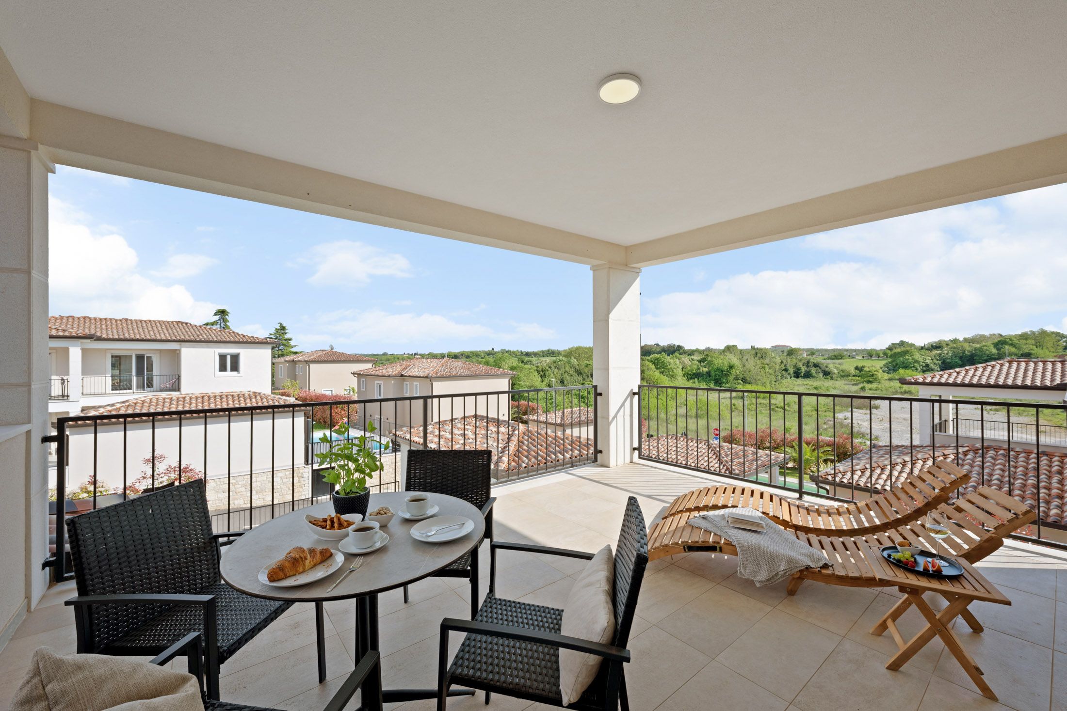 Covered balcony with a breakfast table and lounge chairs overlooking greenery