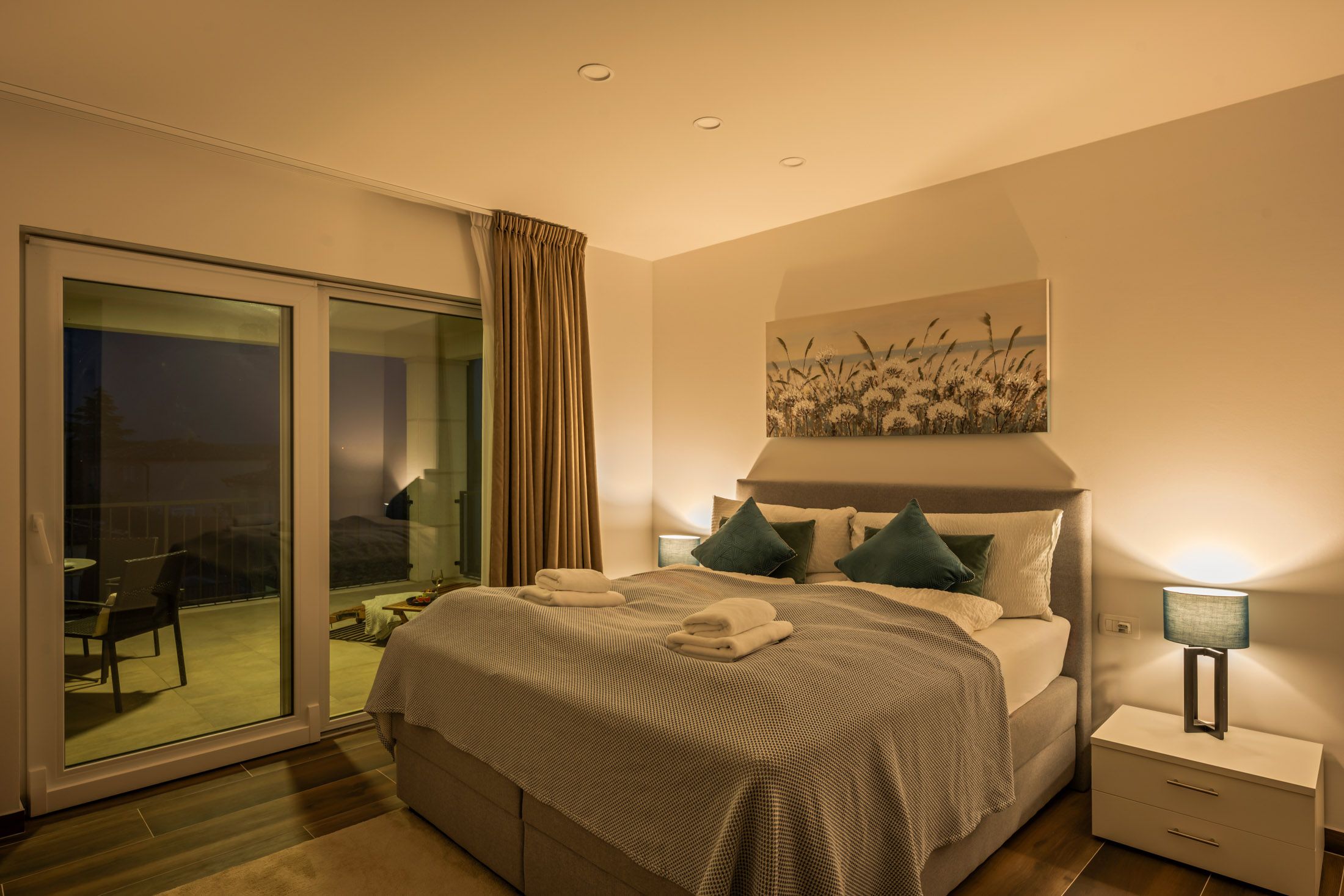 Bedroom in the evening with a made bed and balcony access
