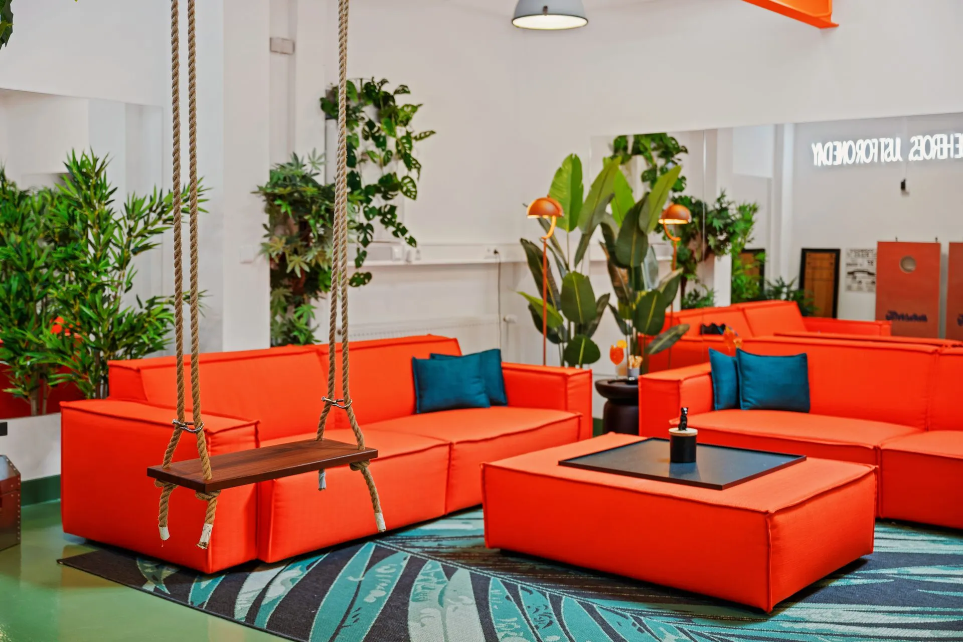 Loft mit orangefarbenen Sofamodulen, Hängeschaukel und großen Grünpflanzen